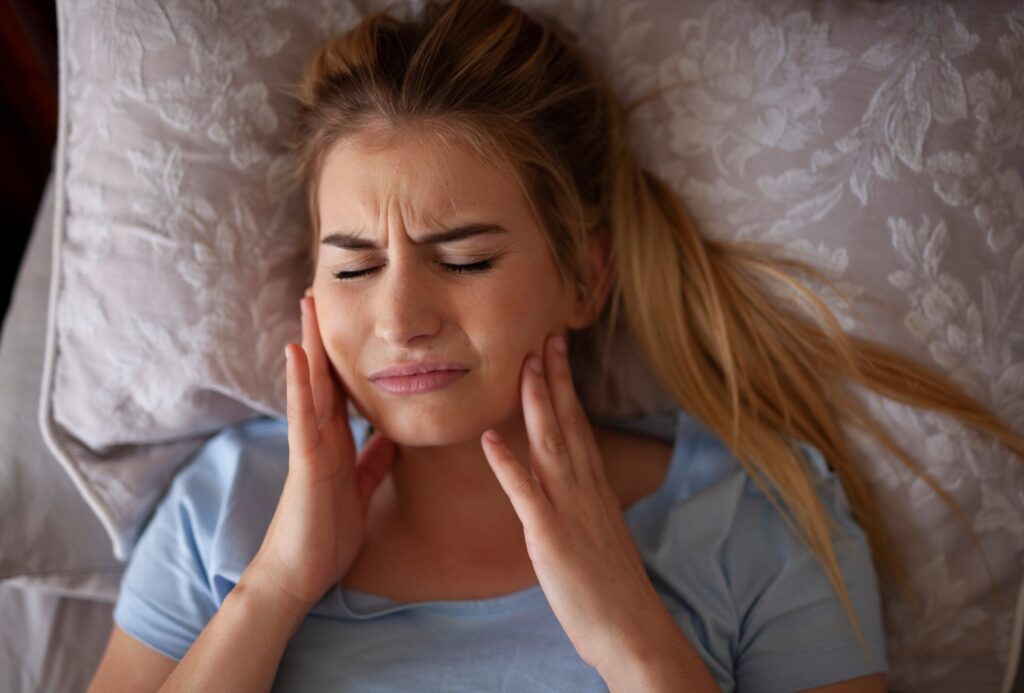 Woman pressing her jaw while lying down, illustrating discomfort from teeth grinding.