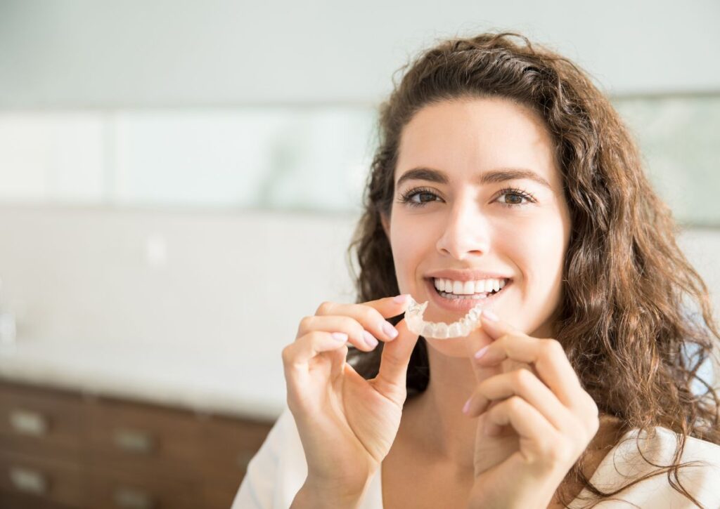 Woman holding clear aligner tray demonstrating Invisalign vs braces treatment in Gympie